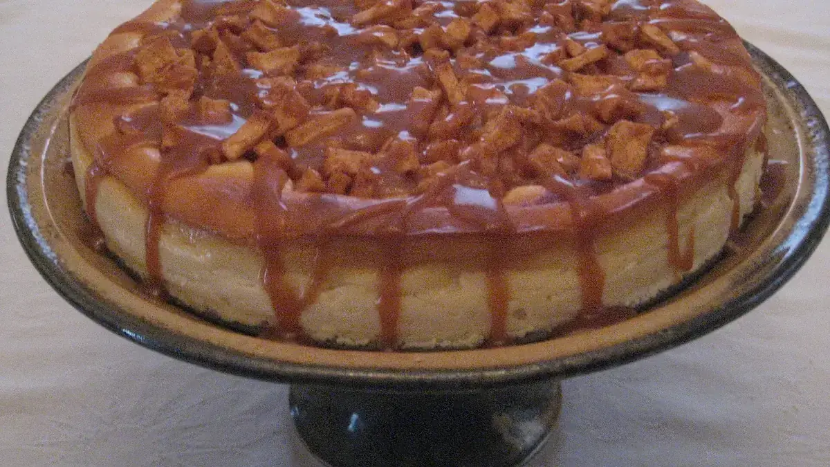 A whole apple caramel cheesecake with caramel drizzle and apple chunks on a cake stand