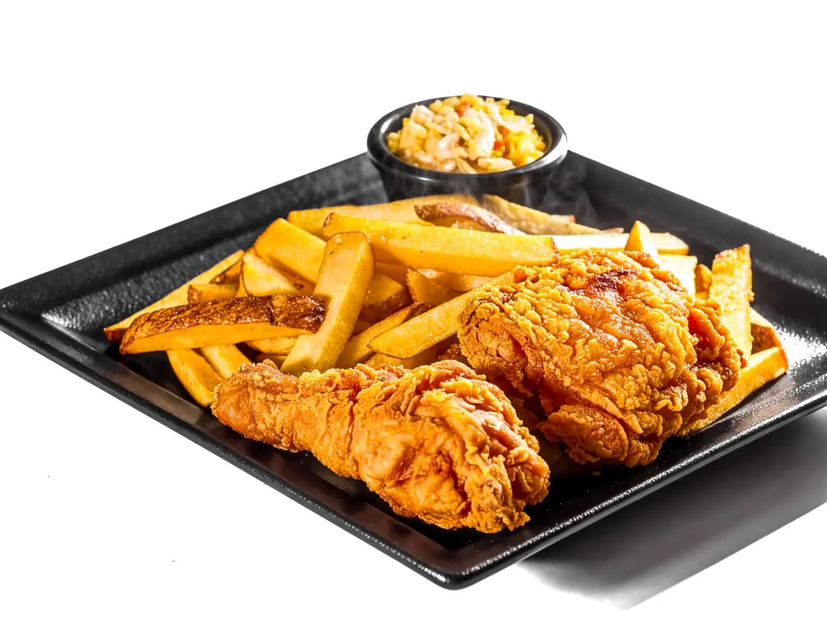Crispy fried chicken pieces with french fries on a black plate
