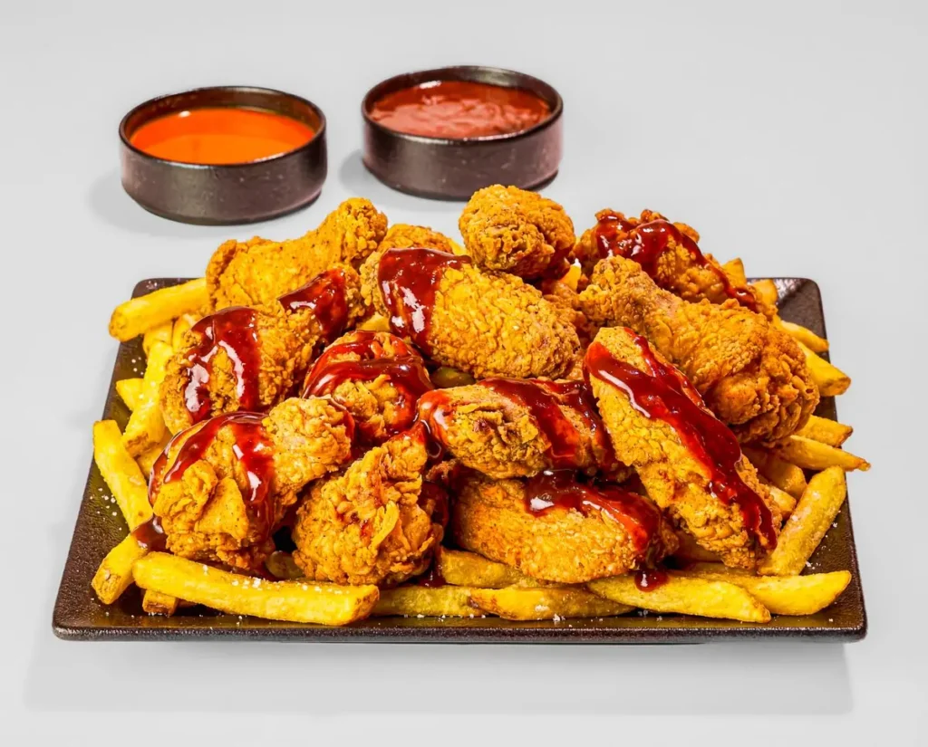 Fried chicken drizzled with red sauce over french fries with dipping sauces