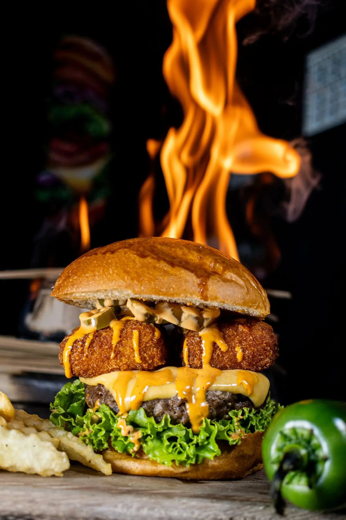 Spicy cheeseburger with jalapeños and cheese sauce in front of flames