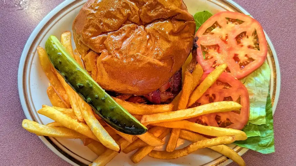 Bacon cheeseburger with french fries, pickle spear, tomato and lettuce on a plate