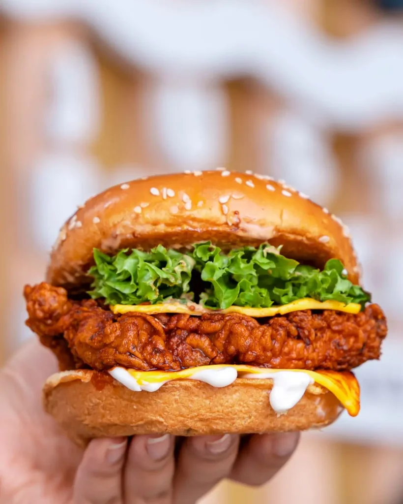 Hand holding a crispy chicken sandwich with lettuce and cheese