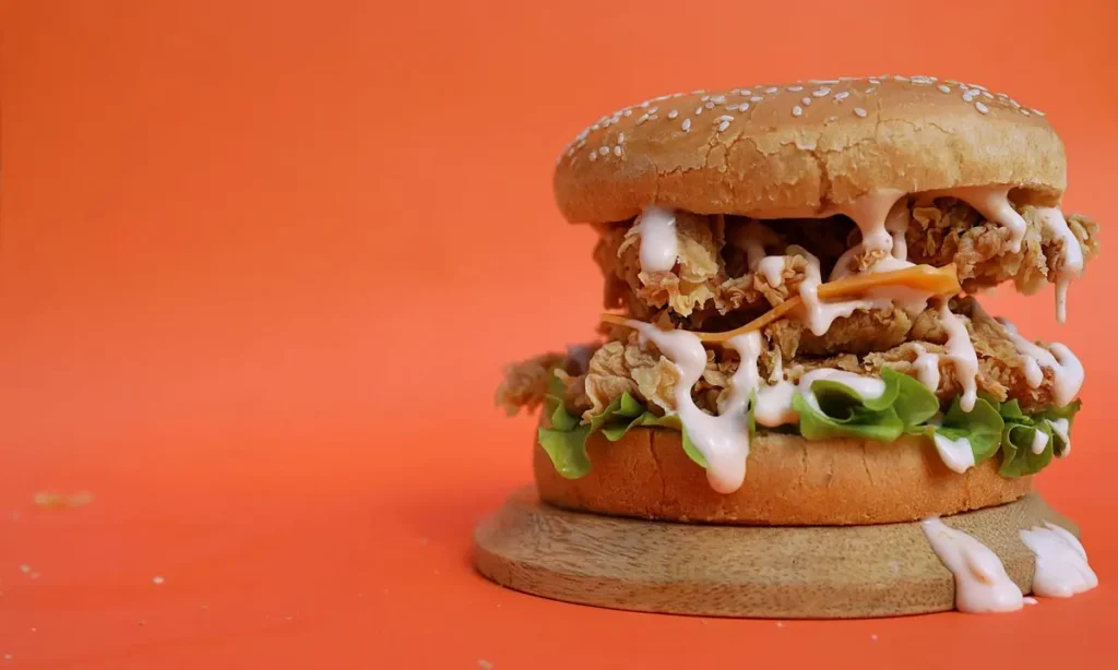 Crispy chicken burger with dripping sauce on an orange background