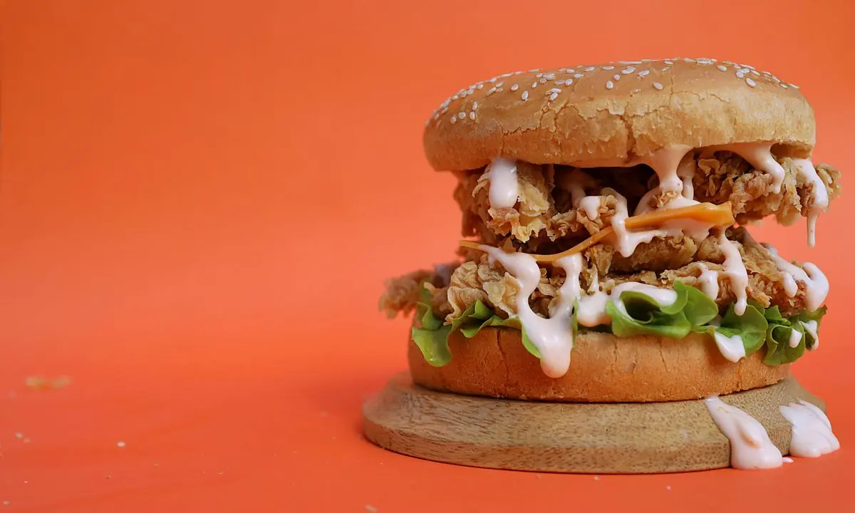 Crispy chicken burger with dripping sauce on an orange background