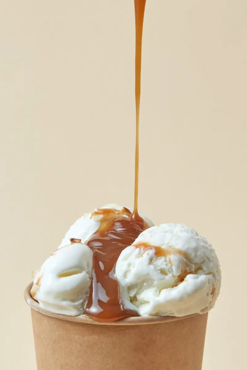 Caramel sauce poured over vanilla ice cream scoops in a cup